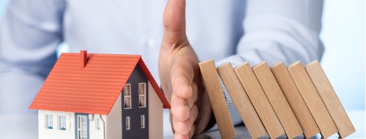 Άνθρωπος σταματά ντόμινο από το να πέσουν πάνω σε μοντέλο σπιτιού με το χέρι του