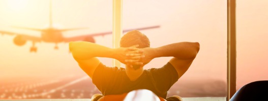 Άνδρας σε αεροδρόμιο κοιτά ξένοιαστος έξω από το παράθυρο όπου αεροπλάνο προσγειώνεται με φόντο το ηλιοβασίλεμα