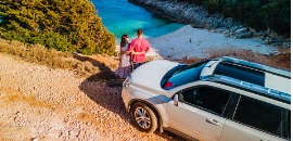 Ζευγάρι μπροστά από το αυτοκίνητό τους αγναντεύουν προς μια παραλία