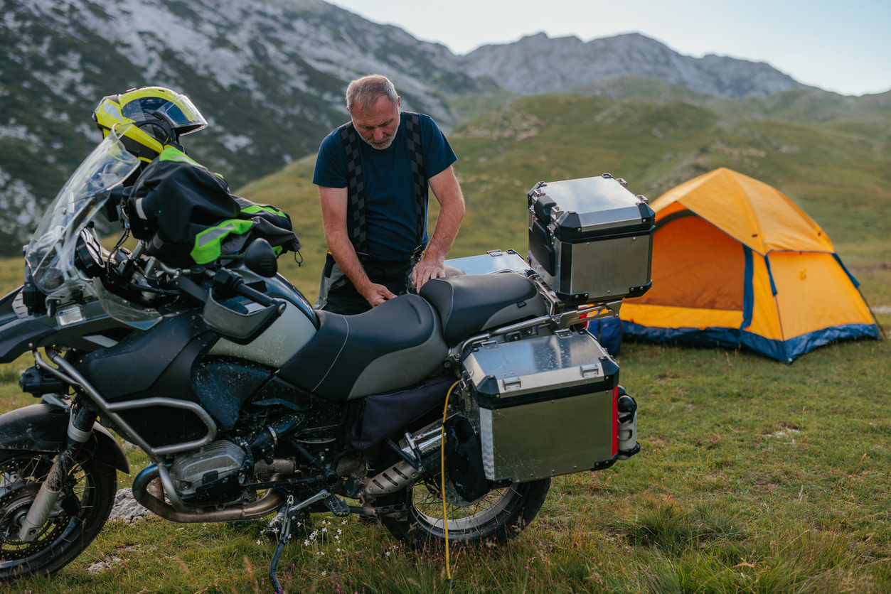 Κατασκηνωτής σε βουνό ξεφορτώνει την touring μηχανή του. Εξοπλισμός camping τριγύρω του