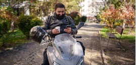 Οδηγός μηχανής πίνει καφέ και βλέπει το κινητό του σταθμευμένος σε πάρκο